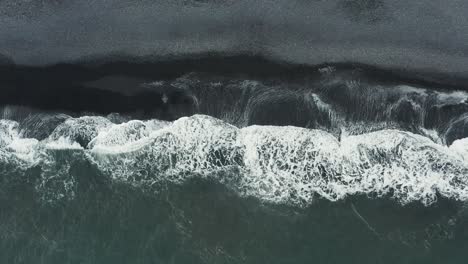 Waves-rolling-onto-shore-of-black-sand-beach-in-Iceland,-aerial