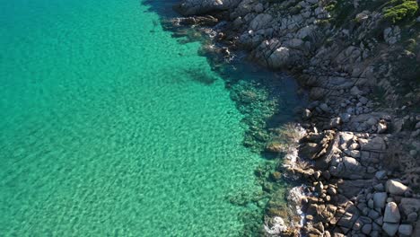 Aerial-shot-of-rocky-cliffside-and-beautiful-clear-turquoise-water-in-South-Sardinia,-Italy