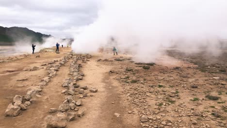 People-photographing-fumarole-with-smoke-from-ground-in-a-desert-environment