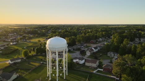 Aerial-orbit-of-a-water-tower-in-suburban-Clarksville,-Tennessee,-revealing-a-beautiful-sunset-at-the-end