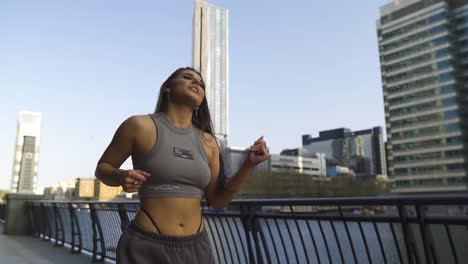 Street-dancer-female-maintain-dancing-while-walking-towards-the-camera-with-confidence-smiling-freestyle-holding-to-the-rail-metropolis-river-bright-sunny-day-slow-motion