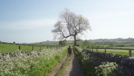 Cámara-Lenta-De-Una-Mujer-Rubia-Caminando-Por-Un-Camino-Rural-Ashbourne,-Peak-District,-Inglaterra