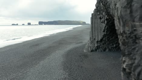 Basalt-cliff-of-Reynisdrangar-at-Reynisfjara-black-beach-and-distant-Dyrhólaey