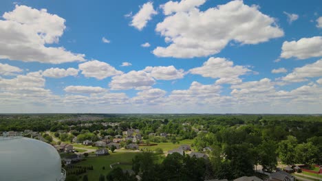 Flying-past-a-water-tower,-revealing-a-beautiful-American-suburb-on-a-gorgeous-sunny-day-with-fluffy-clouds-present
