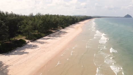 Drone-pan-down-on-beach-in-Chumphon,-Thailand-with-waves-from-the-ocean-along-the-beachfront-with-sand-on-a-sunny-day