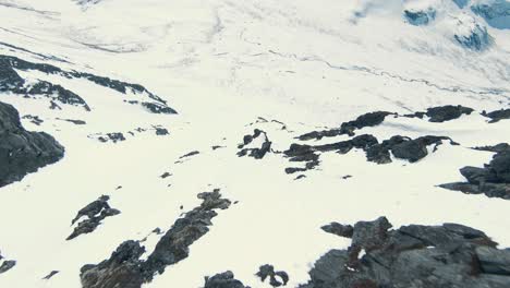 Person-sitting-on-mountain-ridge-on-flying-FPV-drone-in-majestic-winter-landscape