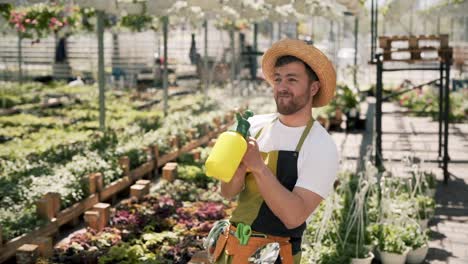 Joyful-adult-male-gardener-in-apron-waters-with-a-sprayer-everything-he-sees