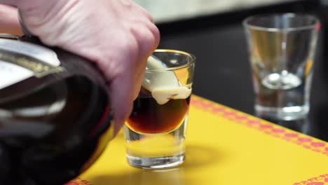 Hands-Pouring-Irish-Cream-Into-Coffee-Liqueur-In-A-Glass-Through-The-Back-Of-A-Cold-Spoon