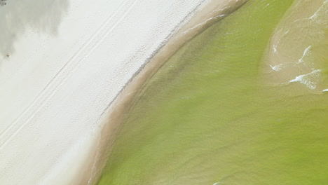 A-summer-beach-on-the-coast-of-Poland,-the-Baltic-Sea-greenish-water-tides-rolling-over-white-sand,-aerial-view