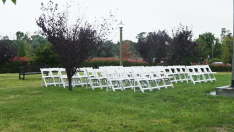 Weiße-Klappstühle,-Die-In-Reihen-Auf-Einem-Grünen-Gras-Angeordnet-Sind,-Das-Für-Eine-Hochzeitszeremonie-Im-Garten-Vorbereitet-Wurde