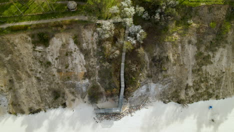 Aerial-view---Stairway-to-walk-down-from-the-cliff-and-people-walking-along-the-baltic-sea-at-the-foot-of-a-cliff-in-Chlapowo,-Poland