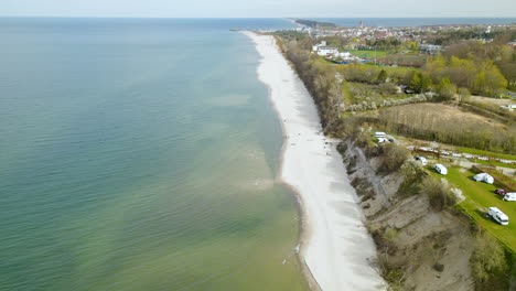 Drone-flying-along-the-baltic-green-sea-beachline-revealing-camping-spots-with-numerous-camper-trailers-on-the-rock-as-well-as-Władysławowo-town-and-Hel-Peninsula-on-background
