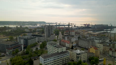 Aerial-view---Gdynia-cityscape-on-a-cloudy-sunset,-marine-cargo-container-port-terminal-on-background