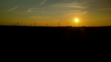Row-of-wind-turbines-spinning-silhouetted-dark-against-golden-sunset-sky