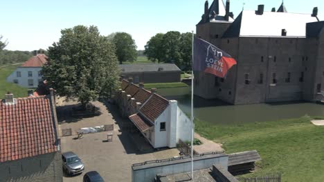Drone-circling-around-flag-of-Castle-Loevestein-revealing-UNESCO-monument-in-the-background-on-a-bright-sunny-day-in-the-Netherlands