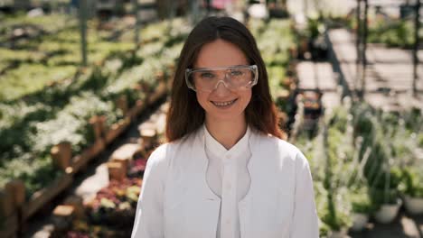 Close-up-portrait-of-a-red-haired-woman-in-a-white-coat-on-a-background-of-greenhouse-plants