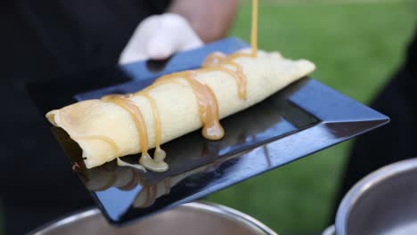 Chef-drizzling-hot-caramel-syrup-sauce-on-crepe,-outdoor-venue-food-service