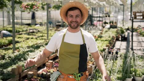Portrait-of-a-young-male-gardener-in-apron-and-hat-looking-at-camera