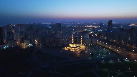 Sharjah:-Vista-Aérea-Temprano-En-La-Mañana-De-La-Ciudad-De-Sharjah,-Mezquita-Del-Rey-Faisal-Iluminada-Durante-El-Amanecer-En-Emirato-árabe-Unido