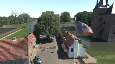 Drone-flying-around-flag-of-Castle-Loevestein-revealing-UNESCO-monument-in-the-background-on-a-bright-sunny-day-in-the-Netherlands