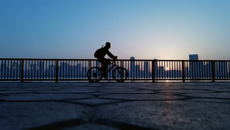 Slow-motion-silhouette:-Ein-Mann-Beim-Radfahren-Mit-Einer-Stadtsilhouette-Im-Hintergrund-In-Sharjah,-Vereinigte-Arabische-Emirate