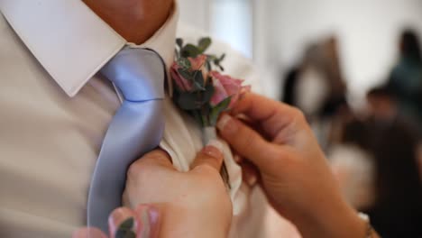 Close-up-shot-showing-groom-getting-wedding-boutonniere-on-white-shirt-during-marriage