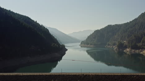 Camper-van-traveling-across-dam-overlooking-Cougar-Reservoir-with-mountains-and-haze-in-background