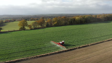A-circling-aerial-shot-of-a-farming-tractor-spraying-a-field-with-sprayer,-herbicides-and-pesticides-on-a-rural-farm