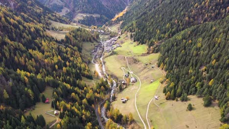 Drone-flying-above-Swiss-village-in-autumn-,-fall-with-mountains-and-a-river-on-the-background