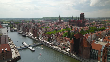 Stunning-Aerial-View-of-Gdansk-Old-Town-District,-People-Crossing-the-Kladka-na-Wyspe-Spichrzow-Bridge-Over-Nova-Motlava-River---drone-pull-back,-St