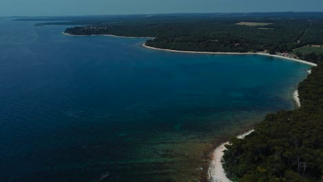 Cinematic-aerial-view-drone-above-a-blue-clear-water-seaside-rock-beach-bay-in-the-idyllic-Adriatic-mediterranean-sea-ocean-in-summer-by-the-Croatian-coast-with-blue-sky-near-Pula-and-Rovinj