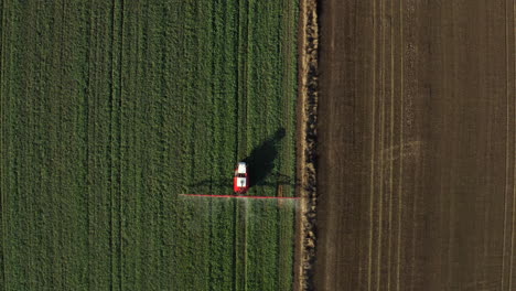An-aerial-topdown-shot-of-a-farming-tractor-spraying-a-field-with-sprayer,-herbicides-and-pesticides-on-a-rural-farm