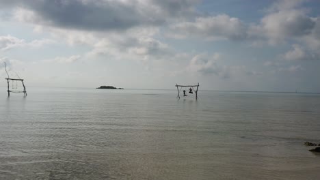 Black-silhouette-of-Two-kids-playing-and-standing-on-wooden-swing-in-the-middle-of-sea-water-at-Karimun-Jawa