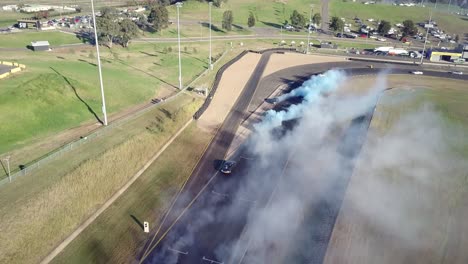 Cars-Racing-On-Asphalt-Race-Track-With-Lots-Of-Smoke-From-Burning-Tires---aerial-shot