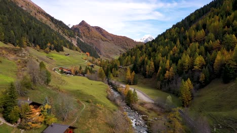 Drone-flying-above-Swiss-village-in-autumn-:-fall-with-mountains-and-a-river-on-the-background