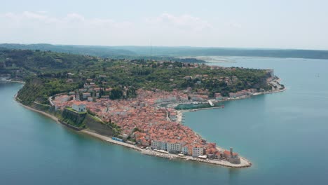 Aerial-arc-shot-circling-high-above-the-city-of-Piran,-Slovenia-on-a-bright-summer-day