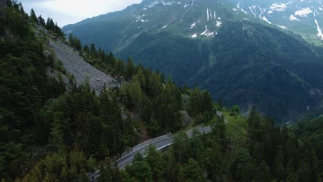 Flying-along-the-idyllic-mountain-cliff-serpentine-road-Plöckenpass-in-the-natural-Austrian-and-Italian-alps-in-summer-with-green-forest-trees-and-blue-peaks