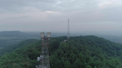 Drone-widely-circling-two-telecommunication-towers-on-top-of-hill-on-foggy-morning