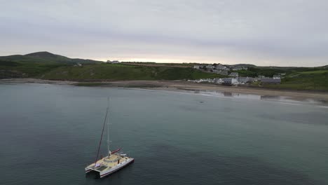 Catamaran-moored-in-bay-at-Aberdaron,-small-town-in-Wales-Aerial-image