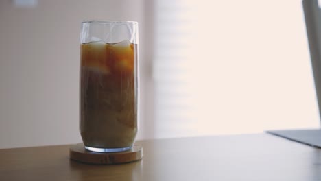 Gießen-Sie-Frische-Milch-In-Ein-Glas-Eiskaffee-Auf-Dem-Tisch-Und-Rühren-Sie-Um