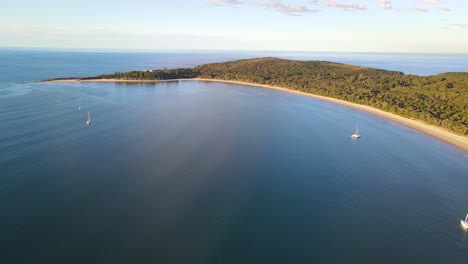 Luftaufnahme-Des-Frontstrandes-Der-Versuchsbucht-Mit-Segelbooten,-Die-Bei-Sonnenuntergang-Im-Blauen-Meer-Fahren---Arakoon-Nationalpark-In-Nsw,-Australien