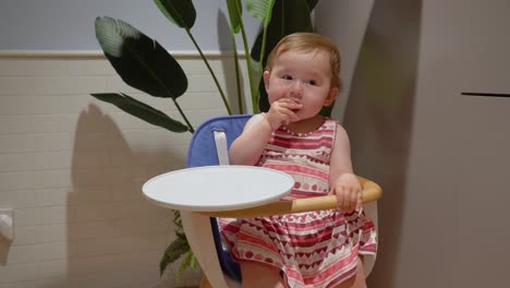 Adorable-baby-girl-eating-snack-and-strike-one's-hand-on-the-table-while-sitting-in-a-wooden-baby-chair