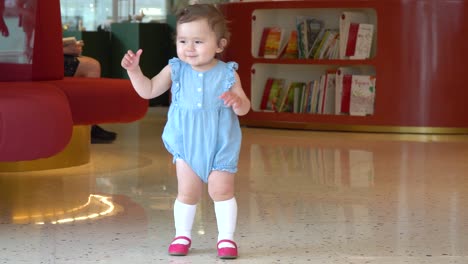 Cute-little-baby-girl-standing-alone-in-a-book-store-and-in-hurry-wobble-to-her-mother-with-laughter