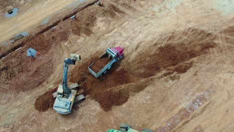 Excavator-loads-dump-truck-at-construction-site---aerial-perspective-in-4K