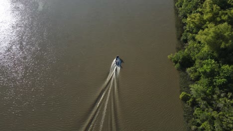 Aerial-flyover-Amazon-River-with-Sun-Reflection-and-riding-boat-near-river-shore-with-rainforest-trees