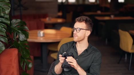 Cute-young-man-with-a-camera-in-a-cafe-looking-at-a-photo