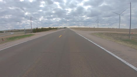 Conduciendo-Por-Una-Carretera-Tranquila-Pasando-Por-Turbinas-Eólicas-En-La-Zona-Rural-Del-Sur-De-Nebraska-En-Un-Día-Nublado-A-Principios-De-La-Primavera