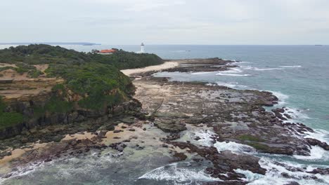 Waves-Crashing-On-Rocky-Coast-Of-Pebbly-Beach-With-Norah-Head-Lighthouse-In-The-Distance---Norah-Head-Headland-In-NSW,-Australia
