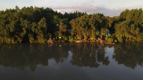 Aerial-tracking-shot-of-beautiful-Amazon-Rainforest-and-lonely-house-on-river-shore-during-sunset-lighting