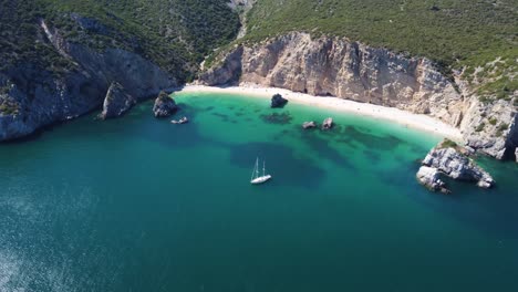 AERIAL-Descending-Fly-By-of-a-Yacht-mooring-at-a-Tropical-Turquoise-Beach-in-Portugal